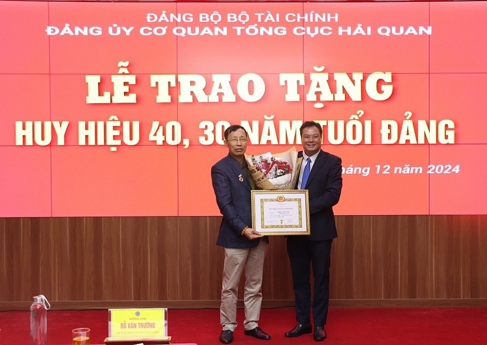 Phó Bí thư thường trực Đảng ủy Bộ Tài chính Đỗ Văn Trường trao Huy hiệu 40 năm tuổi Đảng và tặng hoa chúc mừng nguyên Bí thư Đảng ủy, nguyên Tổng cục trưởng Tổng cục Hải quan Nguyễn Văn Cẩn. Ảnh: Quang Hùng